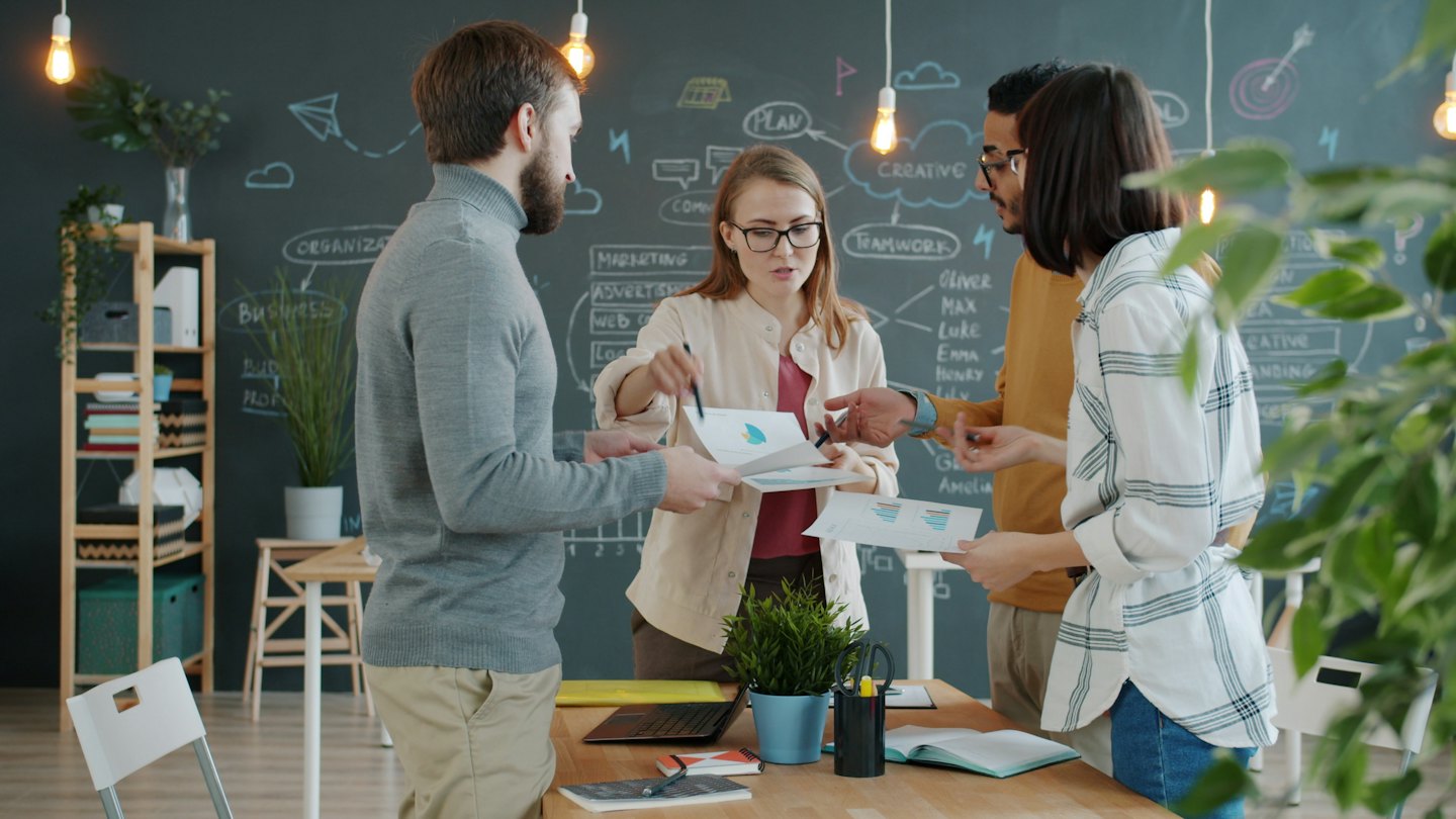 Business team collaborates around a table with charts and diagrams.
